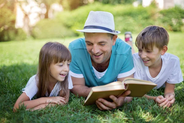 Far Läser Bok För Sina Barn När Han Ligger Utomhus — Stockfoto