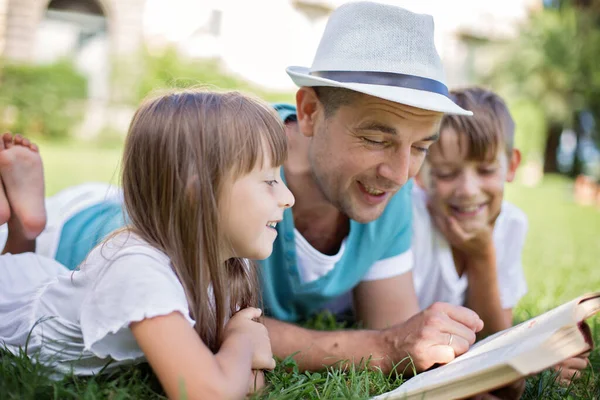 Père Lisant Livre Ses Enfants Pendant Ils Étaient Allongés Dehors Image En Vente