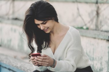 Güzel görünümlü, çok ırklı esmer güzel, zarif, genç ve seksi bir kadının akıllı telefon kullanan portresi. Günlük hayat, moda, güzellik. Kadın portreleri..