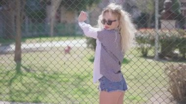 Güzel görünümlü, çok ırklı, sarışın, güzel, seksi, güneş gözlüklü, kısa kot pantolonlu, açık havada poz veren zarif bir genç kadın portresi. Günlük hayat, moda. Kadın portreleri..