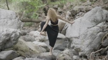 Güzel bir Yogi kadını ormanda eğitim görüyor. Bir bacağı yukarıda, bir bacağı kayanın üzerinde yoga pozu alıştırması. Spor, yoga, esneme, sağlık ve fiziksel egzersiz konsepti. Uyum dengesi etkinliği.