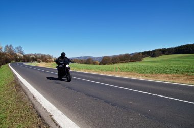 Black motorcycle traveling on the asphalt road in rural landscape in early spring clipart