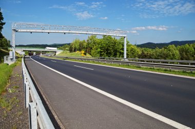 Electronic toll gate over a highway. White trucks and bridge in the background. clipart