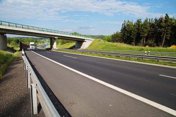 Biały samochód ciężarowy, wprowadzając pod betonowy most nad autostradą w krajobraz zalesionych — Zdjęcie stockowe
