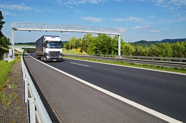 Vit lastbil passerar genom elektronisk toll gates på motorvägen i en trädbevuxen landskap — Stockfoto