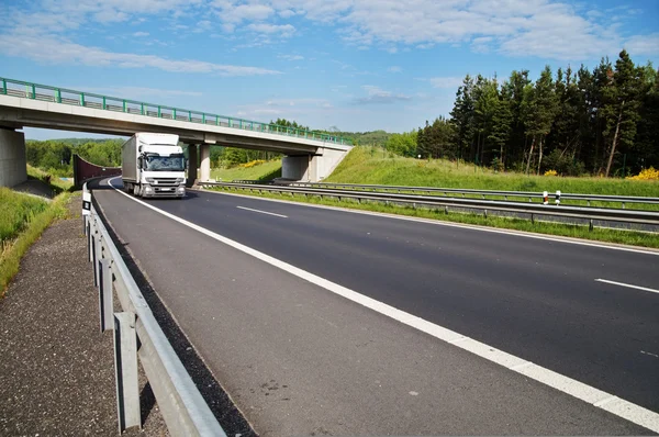 Le camion blanc roule sous un pont en béton sur une autoroute — Photo