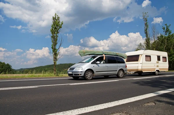 Coche con una canoa en el techo y caravana que viaja por la carretera. Viajar de vacaciones . — Foto de Stock