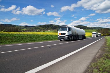 Beyaz tanker ve Sarı çiçekli kolza tohumu alan çevresinde asfalt yol boyunca sürüş kamyon