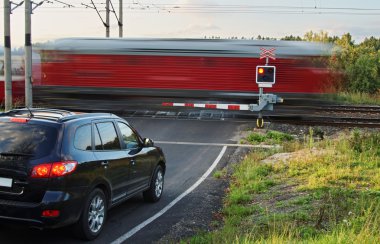 Bir demiryolu geçişi gates ile geçerek hareket bulanıklık kırmızı trenden. Siyah araba ayakta bir asfalt yolda tren engellerin önünde.