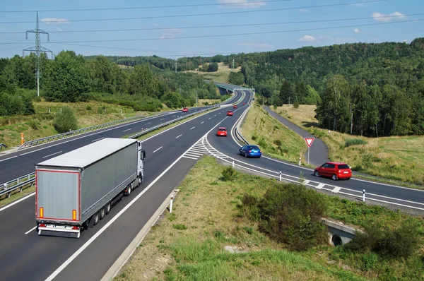 Asfalt karayolu ile beyaz kamyon ve kırmızı binek otomobilleri ormanlık ülke. Geçis kapı uzakta. Yukarıdan görüntüleyin. Mavi gökyüzü gün güneşli yaz.