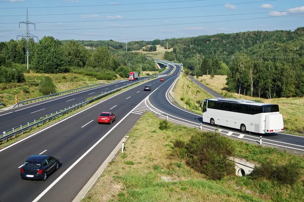 Witte Bus aankomen aan de snelweg van het asfalt op de oprit in een bebost landschap. Rode personenauto's en vrachtwagen rijden op de snelweg. Elektronische tol poort in de verte. Bekijk van bovenaf. Zonnige summ — Stockfoto