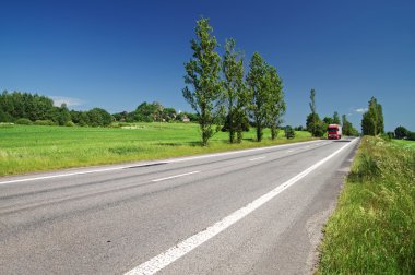 Boş yol kırsalında kırmızı kamyon geçerken mesafe sokakta kavak ile kaplı