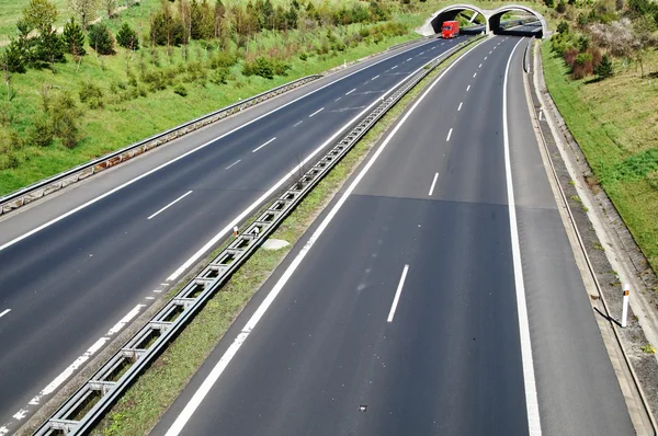 Koridor dálnice s přechodem na přírodu, pod ecoduct červený kamion — Stock fotografie