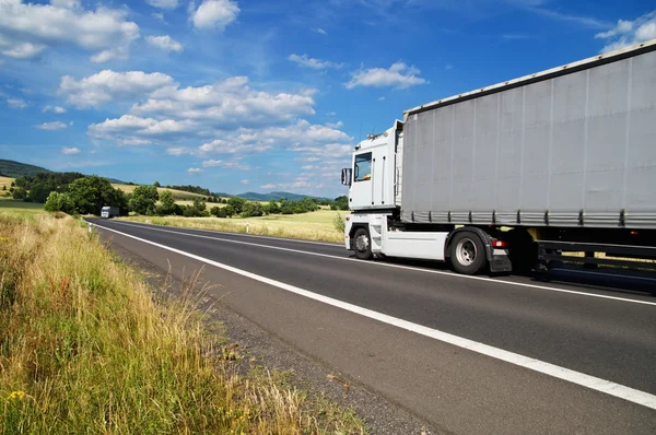 Rural landscape with road and riding a white truck, silver truck in the distance — Stock Photo, Image