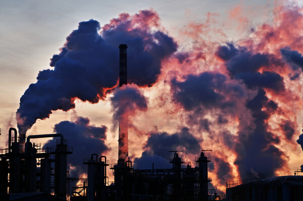 Chimneys and dark smoke over chemical factory at sunset