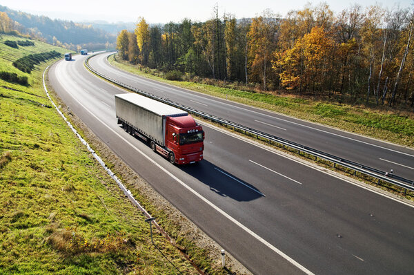 The highway between deciduous forests with leaves in fall colors, the highway ride three trucks