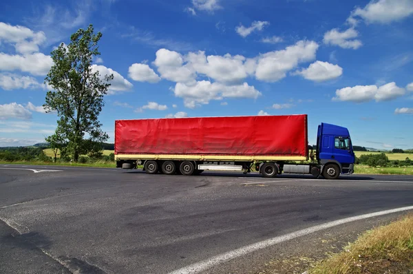 Caminhão azul com vela vermelha passando por uma encruzilhada no campo — Fotografia de Stock