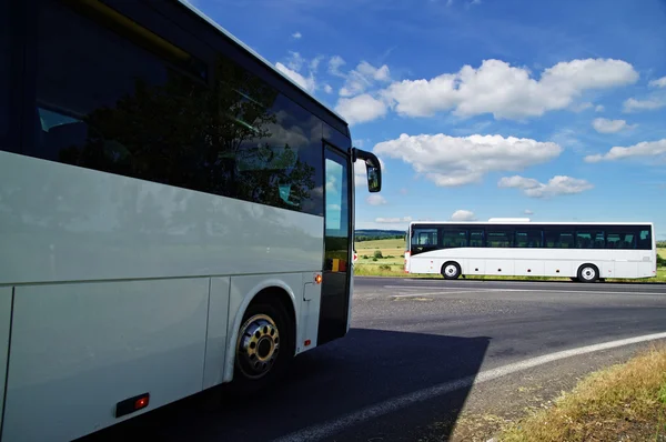Dois ônibus brancos passando pelo cruzamento em uma paisagem rural Imagens De Bancos De Imagens