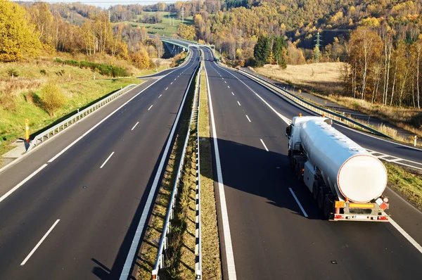 The highway between deciduous trees in autumn colors, white tank, in the distance electronic toll gates and cars — Stock Photo, Image