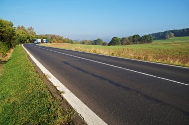 Asphalt road in the countryside, blue and white truck coming around in the distance the bend