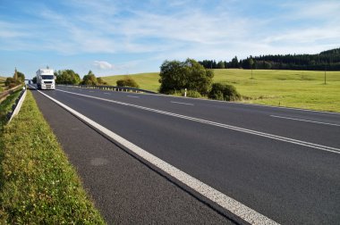 Kırsal manzara içinde asfalt yol. Yolda gelen beyaz kamyon.