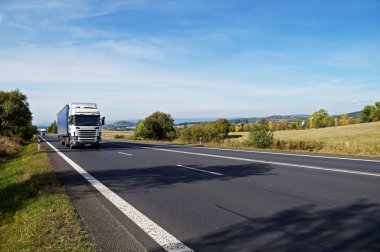 Kırsal manzara içinde asfalt yol. Yolda gelen iki beyaz kamyon.