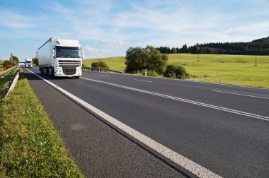 Kırsal manzara içinde asfalt yol. Yolda gelen iki beyaz kamyon.