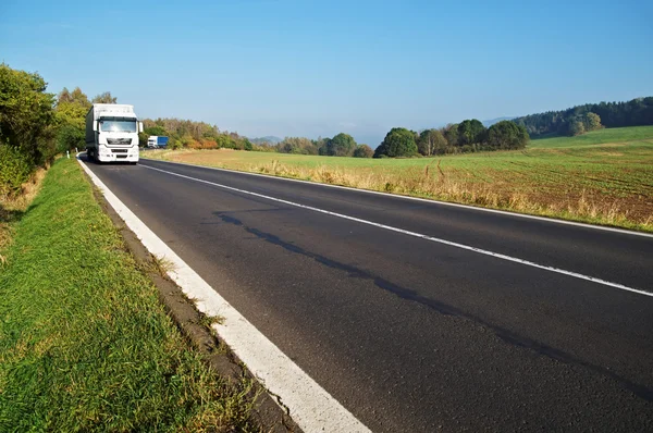 Route asphaltée dans un paysage rural, deux camions — Photo