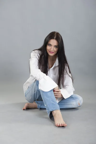 Morena sentada descalza en jeans y una camisa blanca — Foto de Stock