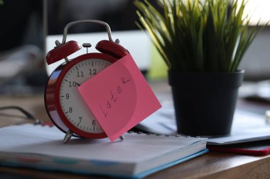 Ofisteki saksının yanındaki masada duran kırmızı alarm saati yakın plan.