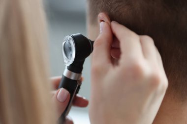 Otorhinolaryngolog elleriyle kulağını çekiyor ve otoskopla yakından bakıyor.
