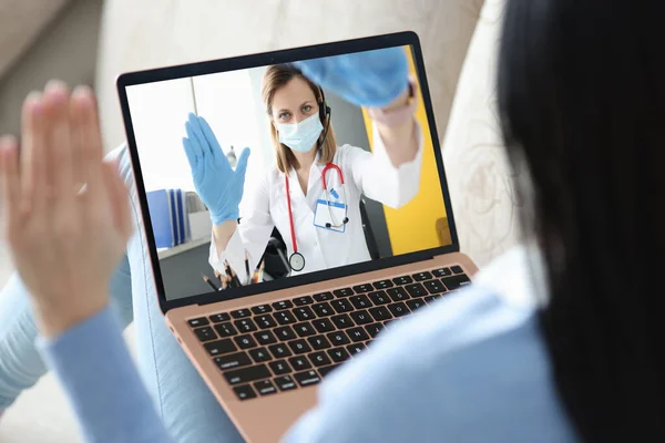 Arzt mit Maske und Handschuhen kommuniziert mit Patient über Laptop Stockbild