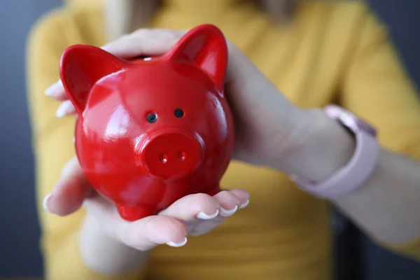 Woman holding red piggy bank in her hands closeup