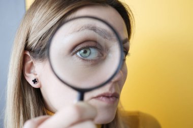 Genç bir kadın gözünün önünde büyüteç tutuyor.