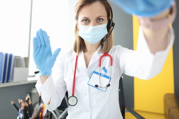 Doctor in protective mask opening lid of laptop and waving his hand