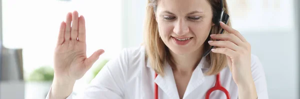 Kobieta lekarz w słuchawkach macha ręką na ekranie laptopa — Zdjęcie stockowe