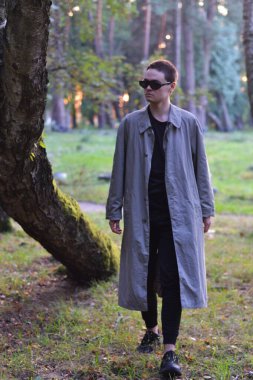 Esmer adam siyah gözlüklü ve gri pelerinli poz veriyor..