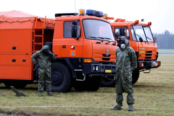 Two men in gas mask and special safe suit for biological danger in front of the orange lorries. Field on background. Biological catastrophe.