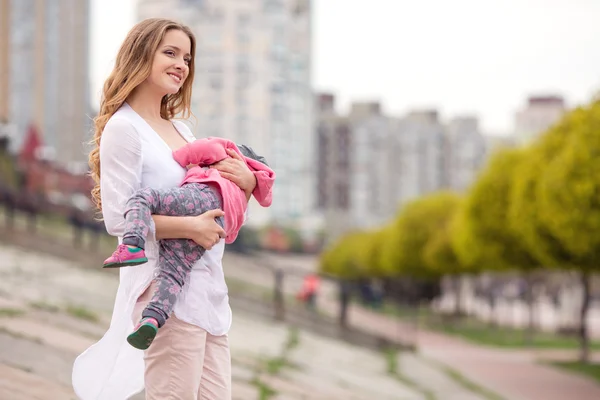 Beautiful young smiling woman with child on urban background — Stock Photo, Image