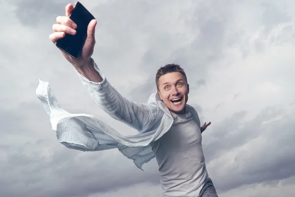 Hombre con un smartphone en la mano. El cielo de fondo con nubes — Foto de Stock