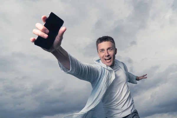 Hombre con un smartphone en la mano. El cielo de fondo con nubes — Foto de Stock