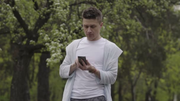 Un giovanotto parla con il cellulare nel parco — Video Stock