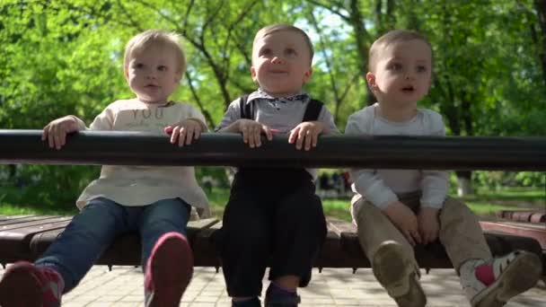 Tres niños felices sentados en un banco en el parque — Vídeos de Stock