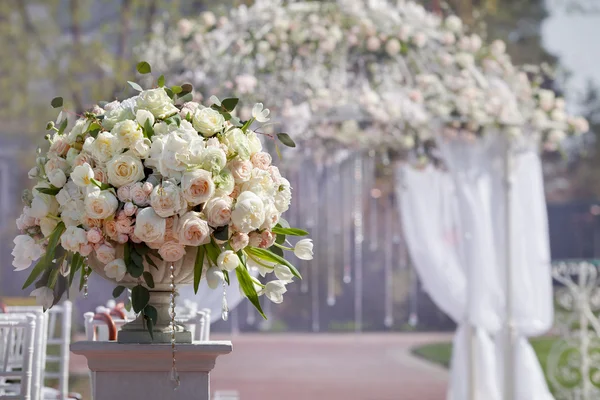 Beautiful bouquet of roses in a vase on a background of a wedding arch. Beautiful set up for the wedding ceremony.