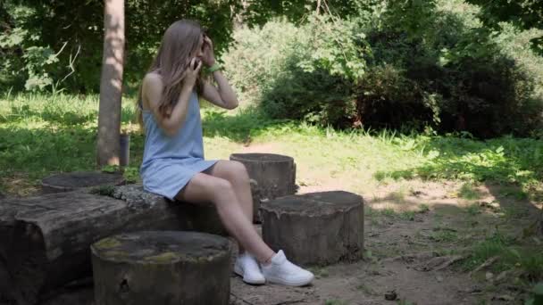 Ung vacker kvinna i en sommarklänning i skogen sitter på stubbe, hon är vilse och ringer räddningstjänsten för att hitta henne — Stockvideo