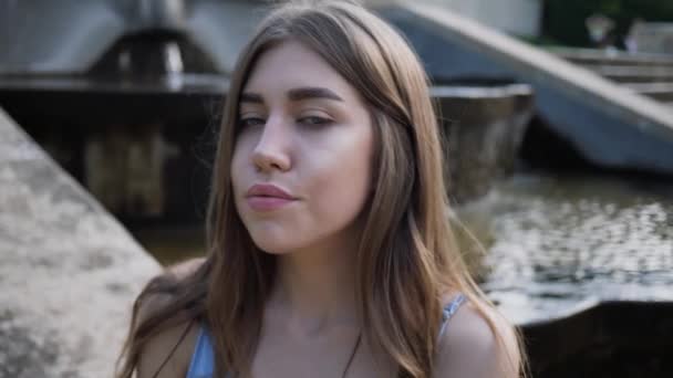 Porträtt av vacker ung kvinna sitter vid fontänen tittar in kameran, ler och väntar på någon. slow motion — Stockvideo