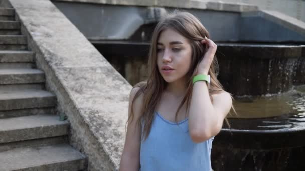 Retrato jovem bela mulher que está esperando para o jovem no parque pela fonte. câmara lenta — Vídeo de Stock