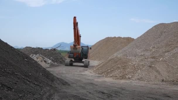 Excavatrice parcourt le site de construction sur fond de montagnes de gravier et de ciel bleu. Russie, Stavropol, 10.06.20 — Video