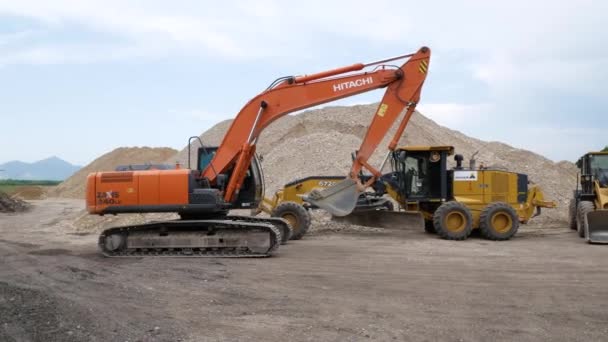 Taş ocağındaki büyük enkaz dağlarına karşı bir inşaat sahasında birçok farklı inşaat ekipmanı var. Kazıcı HITACHI kovayı kaldırıyor. Rusya, Stavropol, 10.06.20 — Stok video