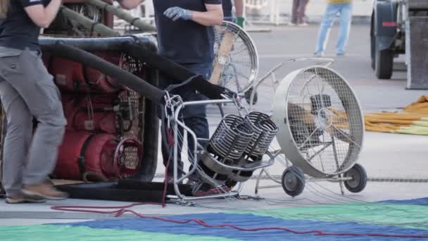 Närbild av upphängd ballongkorg med brännare liggande på marken med gasflaskor och rullad ballong — Stockvideo